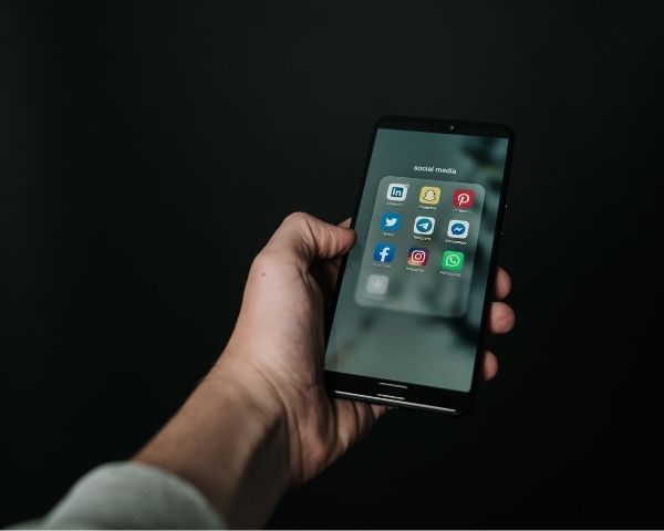 image of a person's hand holding a phone and phone screen have social media app icons